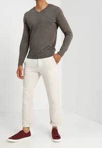 Grauer, gestrickter V-Ausschnitt-Pullover mit langen Ärmeln; kombiniert mit hochgekrempelten, hellen Hosen und burgunderfarbenen Sneakers. Schlichtes, geradliniges Design.