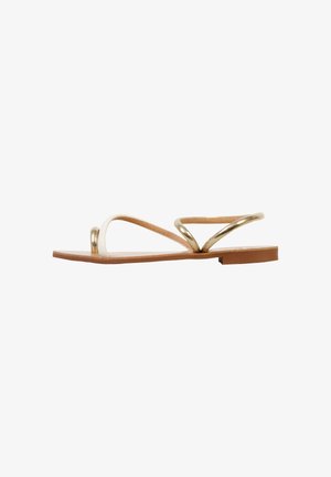 Sandalia plana con suela marrón claro, tira blanca en los dedos y tira metálica dorada en el tobillo sobre fondo blanco.