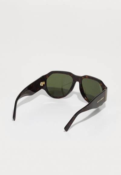 Tarka mintás napszemüveg éles vonalakkal, zöld lencsékkel és arany díszítésű fülpánttal, "DOLCE & GABBANA" felirattal.