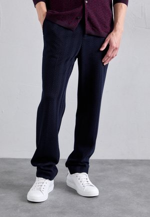Pantaloni navy a motivo a spina di pesce realizzati in un tessuto morbido, dotati di una vita elastica e polsini, abbinati a sneaker bianche.
