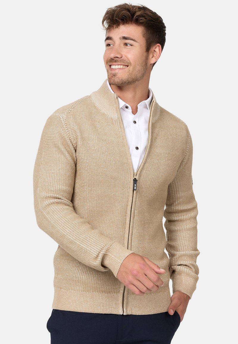 Cardigan beige de cremallera con un patrón de punto texturizado, puños y dobladillo acanalados. Presenta un alto cuello y cremallera frontal para el cierre.