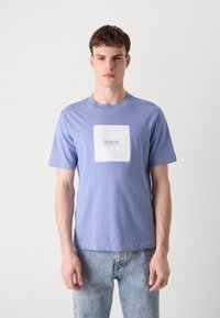 T-shirt de algodão azul claro com um logotipo quadrado branco com o texto "BARBOUR INTERNATIONAL". Manga curta e design clássico de gola redonda.