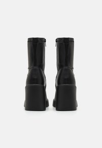 Bottines à talons hauts en cuir noir avec une texture lisse, fermeture éclair et un talon épais pour une stabilité accrue.