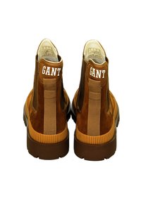 Brown suede ankle boots with elastic side panels, rubber soles, and white "GANT" branding on the heel. Flat, rounded toe design.