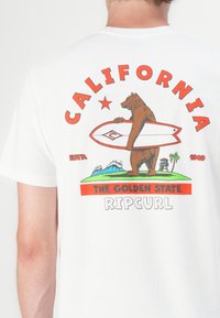 Hvid bomulds t-shirt med et grafisk motiv af en bjørn med et surfbræt, omgivet af teksten: "CALIFORNIA," "THE GOLDEN STATE," og "RIPCURL."
