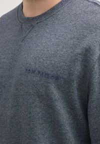 Grijze crewneck sweatshirt van gestructureerde stof, met een subtiele merklogo in donkerblauw op de voorkant.