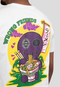 Bílý tričko s barevným grafickým motivem fialové postavy s nudlemi v misce, textem "ŠPATNÍ PŘÁTELÉ" a dekorativními akcenty.