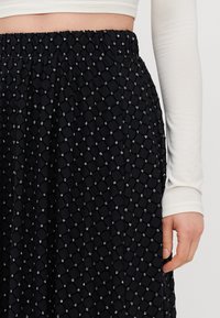 Svart skjørt med en strukturert diamantmønster, dekorert med små rhinestones. Elastisk liv gir komfort og enkel bruk.