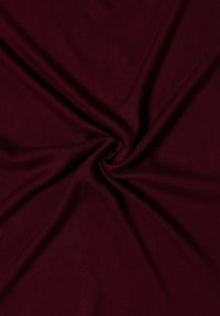 Tissu bordeaux profond torsadé au centre, créant des plis doux et des variations de texture sur la surface lisse.