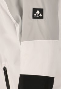 Hvid, grå og sort jakke med en glat tekstur. Har lynlåse, et logo patch på ærmet, og farveblokkerede sektioner.