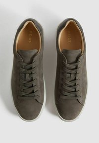 Sneakers din suede gri închis cu vârf rotund, șireturi plate verzi și tălpi de cauciuc crem. Interiorul are căptușeală din piele bej. Numele brandului este vizibil.