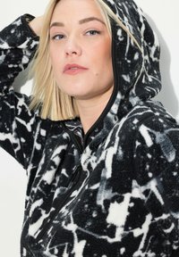 Czarny i biały polarowy hoodie w wzory z zamkiem błyskawicznym, z kapturem i kontrastowym czarnym wykończeniem na zamku oraz mankietach.