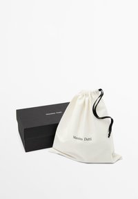 Sort Massimo Dutti skotape ved siden af en hvid stofpose med snor i sort og mærkenavn på fronten.