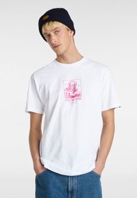 Hvid bomulds t-shirt med et pink grafisk design af et skelet, der læser, med teksten "READ THE ROOM." Kombiner med denimbukser og en marineblå beanie.