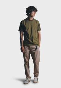 Camiseta verde oliva de mangas cortas y escote redondo, combinada con pantalones beige claros y zapatillas blancas con rayas negras.