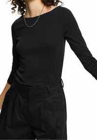Czarny top z długim rękawem i okrągłym dekoltem, zestawiony z czarnymi spodniami o wysokim stanie z fałdami. Srebrny naszyjnik z łańcuszkiem dopełnia stylizację.