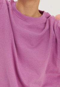 Sudadera morada con una textura suave, cuello redondo y ribete de canalé. La tela parece ligeramente drapeada, mostrando un color suave y uniforme.