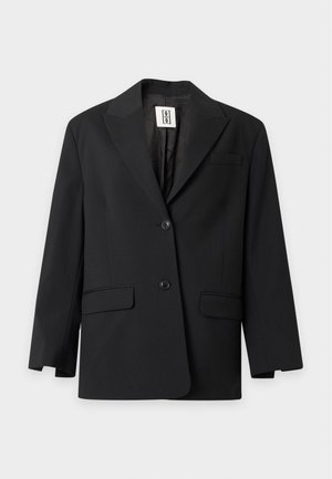 Kvinde iført oversized sort blazer, hvid t-shirt med tekst, beige vidde bukser med høj talje og mørkebrune højhælede sko.