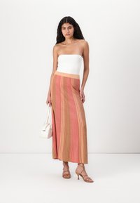Jupe maxi avec des rayures verticales rose et dorées, tissu texturé, taille haute, associée à un haut bustier blanc et des sandales nude.