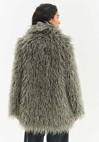 Płaszcz z futerka sztucznego w stonowanym zielonym kolorze z puszystą, teksturowaną powierzchnią oraz luźnym, oversize'owym krojem. Wysoki kołnierz i długie rękawy.