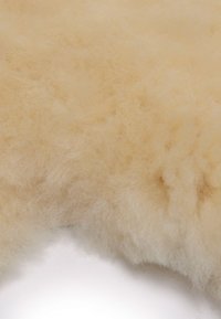 Schaffellteppich, weiche Textur, blassbeige Farbe, flauschige Oberfläche, natürliche Fasern, undefinierte Kanten, leichter Glanz, einheitliche Dicke.