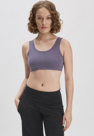 Lila Crop-Top mit Rundhalsausschnitt und breiten Trägern, aus weichem Stoff. Kombiniert mit schwarzen hochtaillierten Hosen. Einfaches Design, ohne Muster.