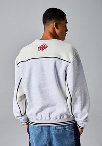 Grijze sweatshirt met crèmekleurige schouderpanelen, zwarte piping, ribgebreide manchetten en een rode vlamgrafiek op de achterkant. Geweven stof, relaxed fit.