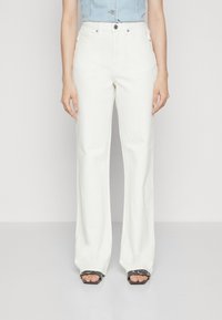 Jean blanc à jambes larges avec une texture lisse, taille haute et design minimaliste. Assorti de sandales compensées noires avec une boucle argentée.