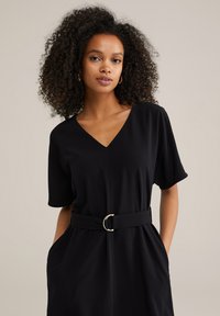 Robe noire en matériau doux, avec un col en V, des manches courtes, une taille cintrée avec une ceinture et des poches latérales.