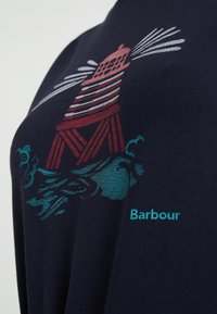 Granatowy materiał z czerwono-białym paskowanym latarnią morską oraz niebieskimi falami, a po prawej stronie napis "Barbour" w kolorze teal.