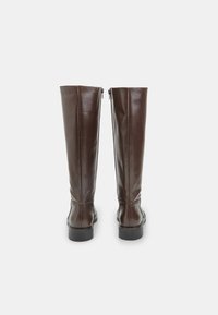 Botas de cuero marrón hasta la rodilla con una textura suave, que cuentan con un cierre de cremallera en la parte trasera y una suela plana, diseñadas para una silueta ajustada.