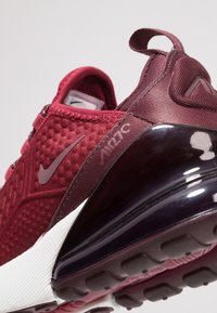 Detailní záběr na bordó tenisku Nike Air Max 270, se zvýrazněným texturovaným svrškem, poutkem na patě a viditelnou vzduchovou tlumící podrážkou.
