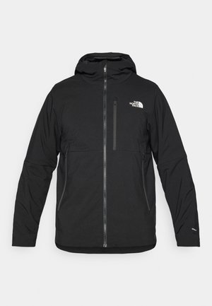 Svart hettejakke laget av teksturert stoff, med glidelås foran, en brystlomme og en logo på øvre venstre side.