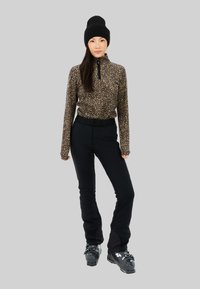 Haut zippé en imprimé léopard, pantalon de ski noir et bonnet en tricot noir. Bottes de ski noires brillantes avec du matériel réglable. Textures lisses tout au long.