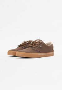 Brown canvas sneakers with rubber soles, round-toed design, contrasting tan laces, and subtle logo on the side.