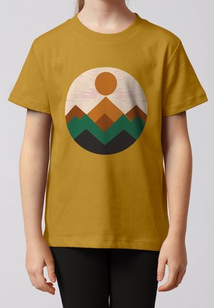 Kind trägt senfgelbes T-Shirt mit rundem Aufdruck von stilisierten Bergen in Braun, Grün und Schwarz unter einer orangefarbenen Sonne.