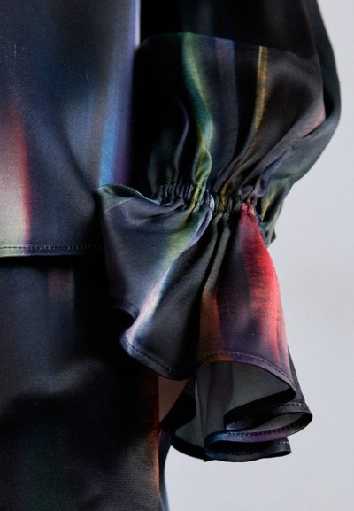 Blusa multicolore con una texture seta. Presenta un volant arricciato al polsino e un mix di tonalità scure con strisce vivaci.