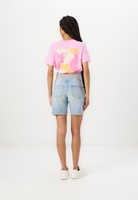 Růžové tričko s květinovým potiskem na zádech, doplněné světle modrými džínovými šortkami. Modelka má na sobě bílé tenisky. Jednoduchý, ležérní outfit.