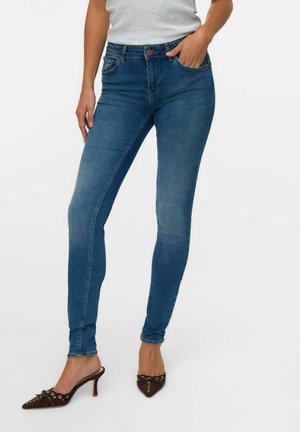 Jean skinny bleu en denim, avec une taille mi-haute, cinq poches et une légère décoloration. Associés à des escarpins bruns à bout pointu.