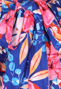Tessuto blu a fantasia floreale con foglie rosa, rosse e azzurre. Presenta un design con vita annodata realizzato in materiale morbido e strutturato.