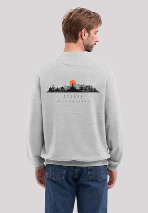 Grauer Sweatshirt mit einem grafischen Druck einer Skyline und einer Sonne, mit einem lockeren Schnitt und gerippten Bündchen. Sichtbare Nähte an der Jeans.