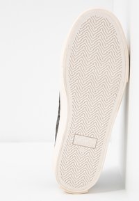 Černá vzorovaná podrážka tenisky s bílou gumovou podrážkou, která má cik-cak vzor a na patě je embosovaný logo "NO NAME".