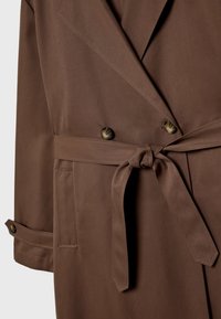 Bruine double-breasted jas met een gebonden ceintuur, grote ingesneden revers en zijzakken met knoopdetails op de mouwen. Gladde stoftextuur.