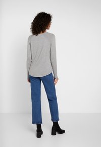 Graues Langarmoberteil mit abgerundetem Saum, getragen mit blauen geraden Jeans und schwarzen Stiefeletten, mit gerippten Bündchen und Kragen.