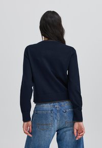 Suéter recortado azul marino hecho de tela de punto, con puños y dobladillo acanalados, combinado con jeans de mezclilla de tiro alto con bolsillos traseros.