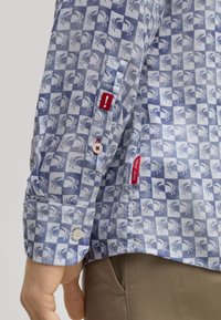 Camicia a quadri blu e bianca con design a scacchi e grafiche di granchio, polsini con bottoni e accenti rossi del logo. Materiale in cotone.