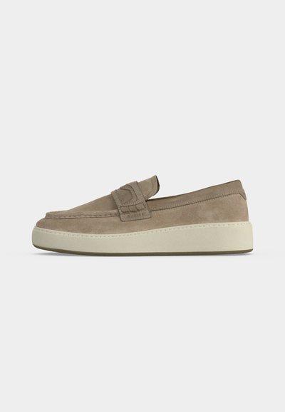 Mocassin beige en daim à enfiler avec une semelle blanche épaisse et un détail de sangle sur le dessus, présenté en profil latéral sur fond blanc.