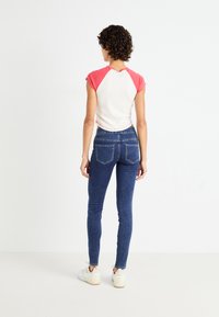 Bílý a růžový top s krátkými rukávy a raglánovými rukávy, který je spárován s tmavě modrými skinny džíny s dvěma zadními kapsami a roztrženým lemem.