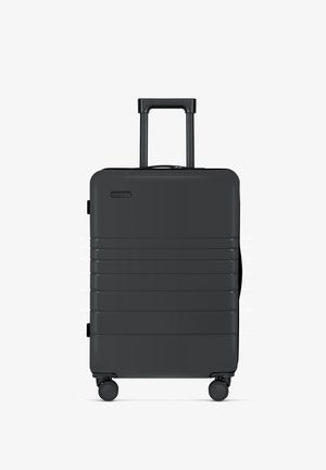 Zwarte harde koffer met verticale ribbels, uittrekbare handgreep en vier wielen voor gemakkelijke mobiliteit. Compact ontwerp met ritssluiting.