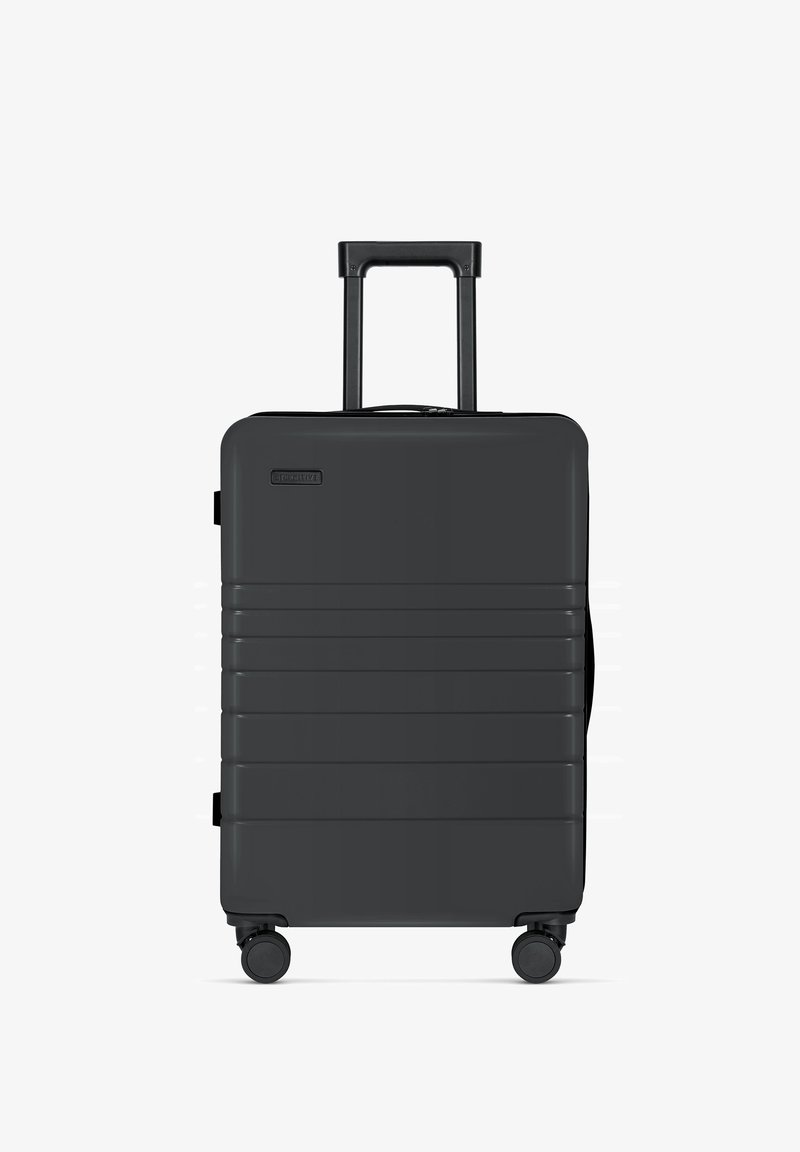 Zwarte harde koffer met verticale ribbels, uittrekbare handgreep en vier wielen voor gemakkelijke mobiliteit. Compact ontwerp met ritssluiting.